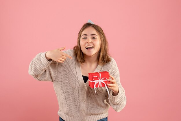 молодая женщина держит маленький рождественский подарок на розовом