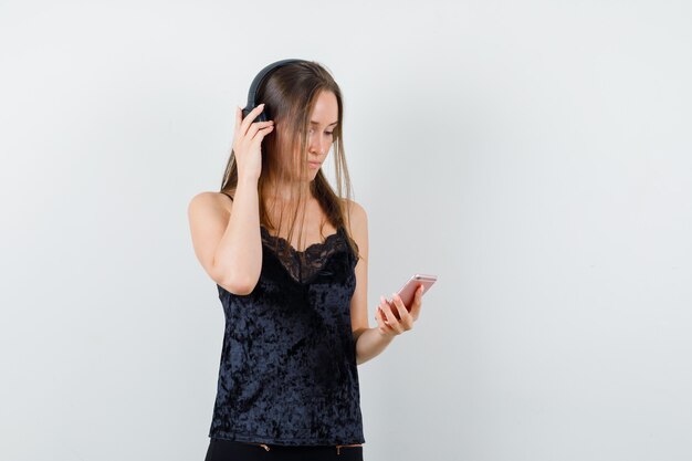 Young female holding mobile phone, listening to music in black singlet