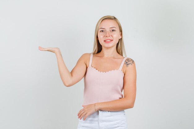 Young female holding open palm in singlet, mini skirt and looking cheerful.