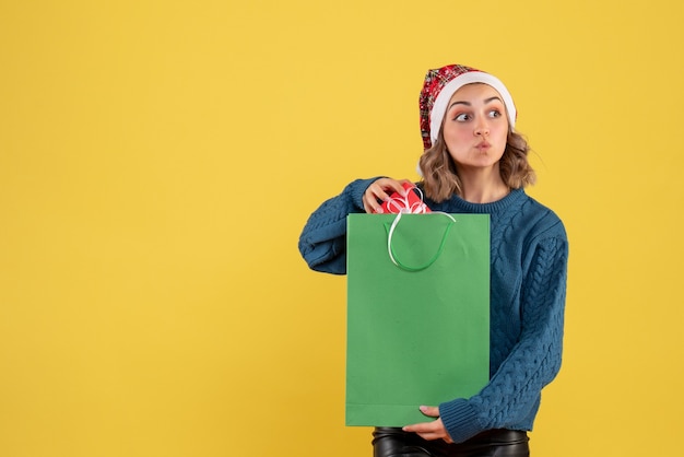 Бесплатное фото Молодая женщина держит пакет и маленький подарок на желтом