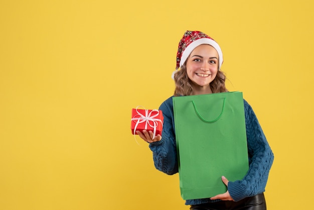 молодая женщина держит пакет и маленький подарок на желтом