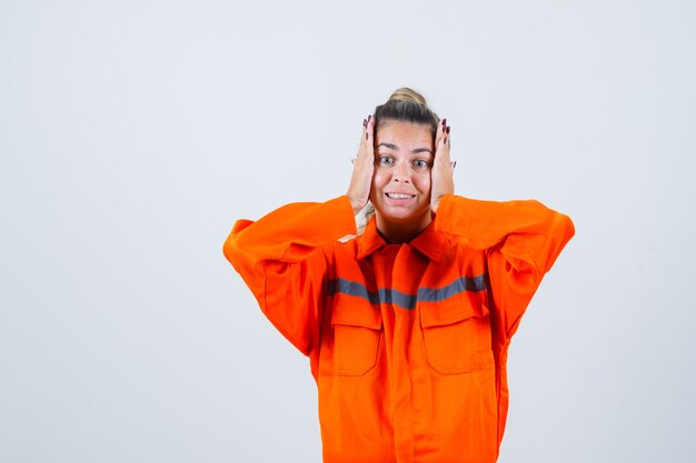 Young female holding palms on her cheeks in worker uniform and looking uncomfortable. front view.