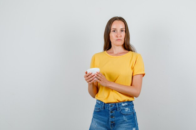 Young female holding pencil holder in t-shirt, shorts and looking serious. front view.