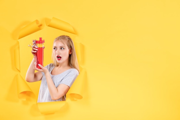Young female holding red bottle on a yellow wall