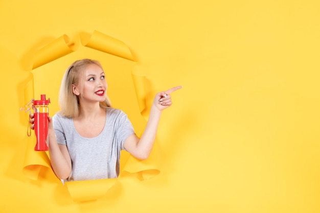 Free photo young female holding red bottle on yellow wall