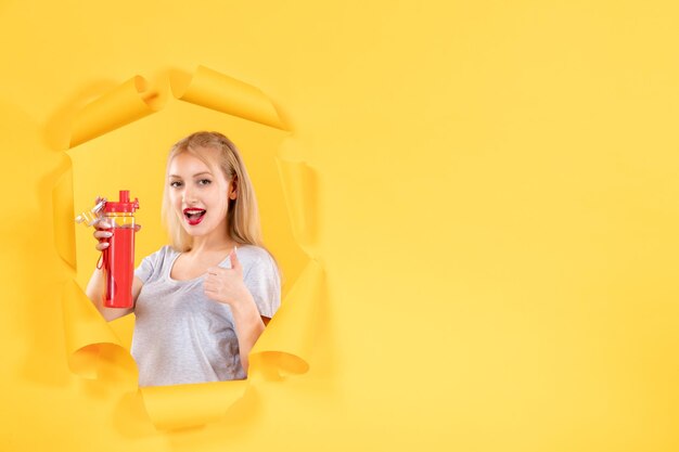 Young female holding red bottle on yellow wall