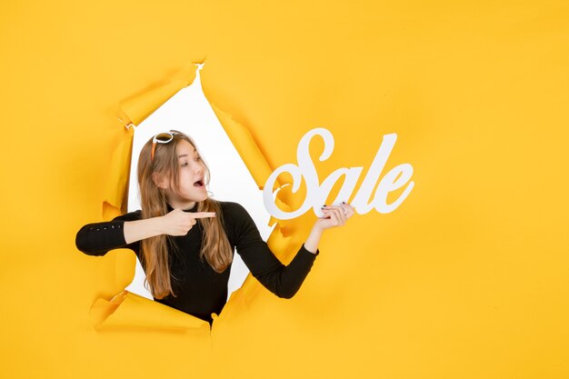young female holding sale writing through torn paper hole in the wall