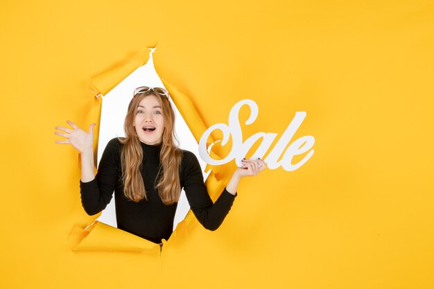 Young female holding sale writing through torn paper hole in the wall