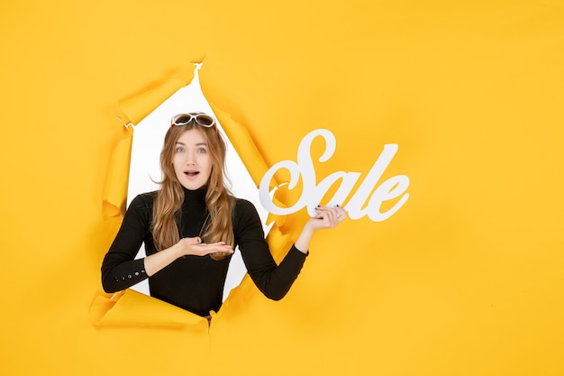 young female holding sale writing through torn paper hole in the wall