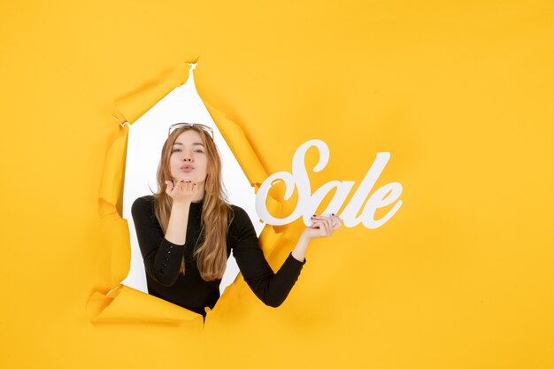 Young female holding sale writing through torn paper hole in the wall