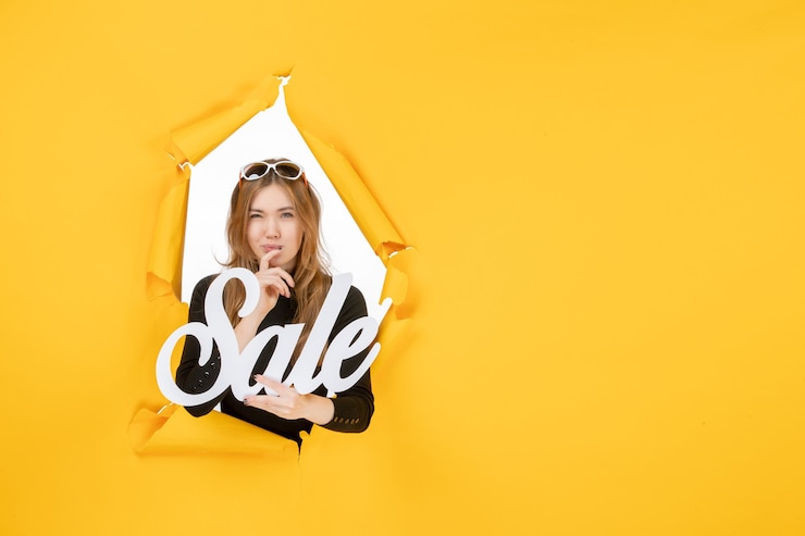 Free Photo young female holding sale writing through torn paper hole in the wall