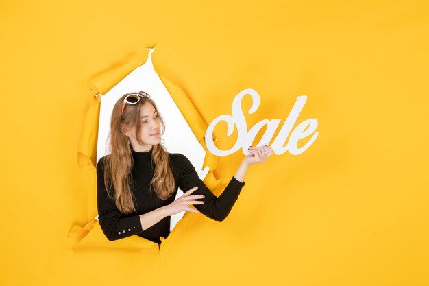 Young female holding sale writing through torn paper hole in the wall