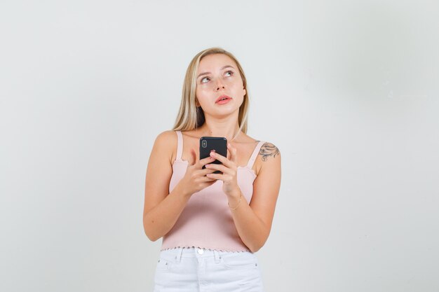 Молодая женщина держит смартфон и смотрит в синглет, мини-юбку.