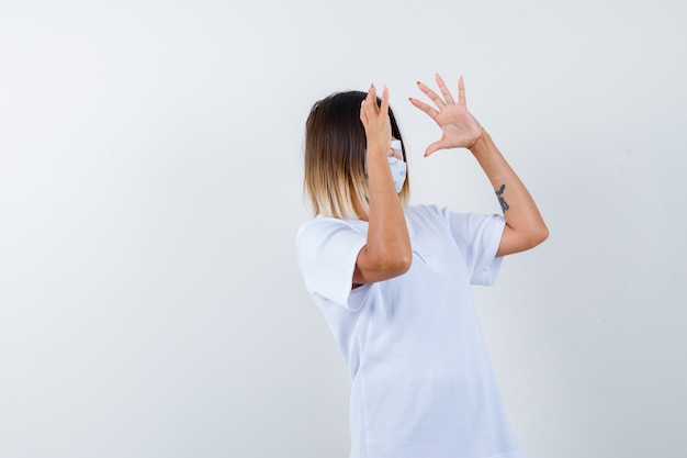 Foto gratuita giovane donna che tiene qualcosa in t-shirt, maschera e sembra sicura. vista frontale.