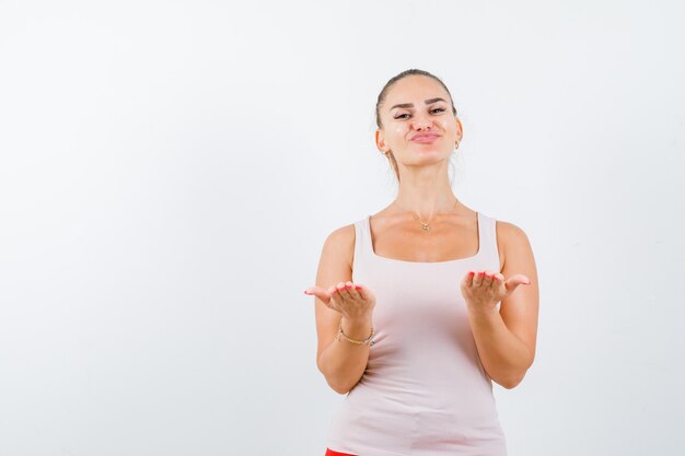 Young female holding something in white tank top and looking positive. front view.