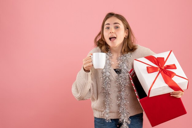 young female holding xmas present box and cup of tea on pink