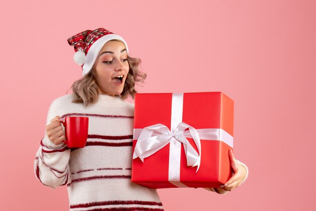 クリスマスプレゼントとピンクのお茶を保持している若い女性