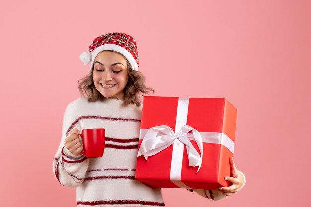 молодая женщина держит рождественский подарок и чашку чая на розовом