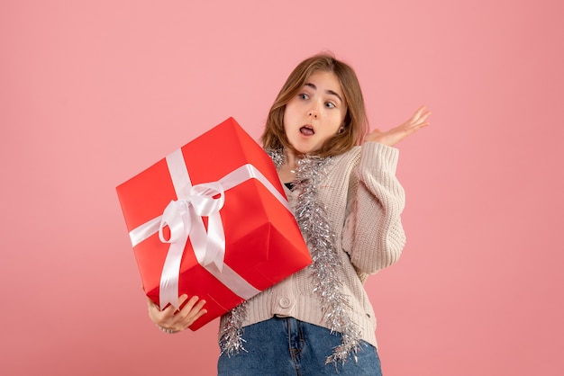 Young female holding xmas present in her hands on pink