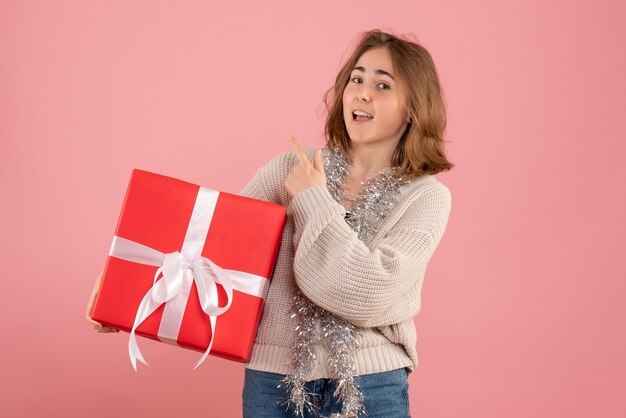 Бесплатное фото Молодая женщина держит в руках рождественский подарок на розовом