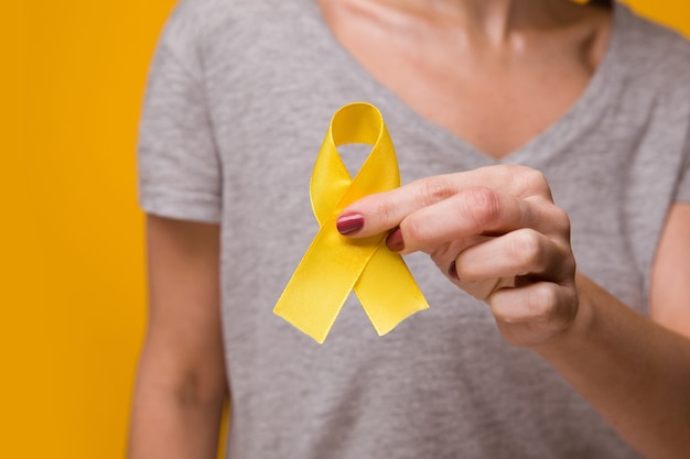 Young female holding yellow gold ribbon awareness symbol for endometriosis, suicide prevention, sarcoma bone cancer, bladder cancer, liver cancer and childhood cancer concept. health care. close up.
