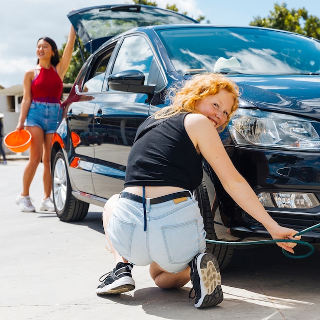 Young female inflating tire of automobile while other woman closing trunk in background