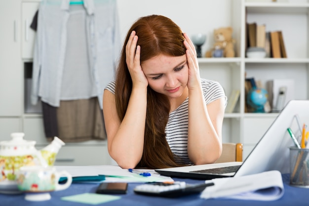 La giovane femmina è seduta al tavolo e ha problemi con il lavoro