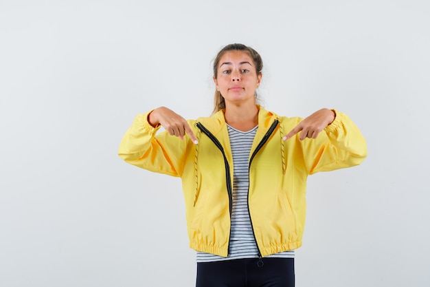 Young female in jacket, t-shirt pointing down and looking confident , front view.