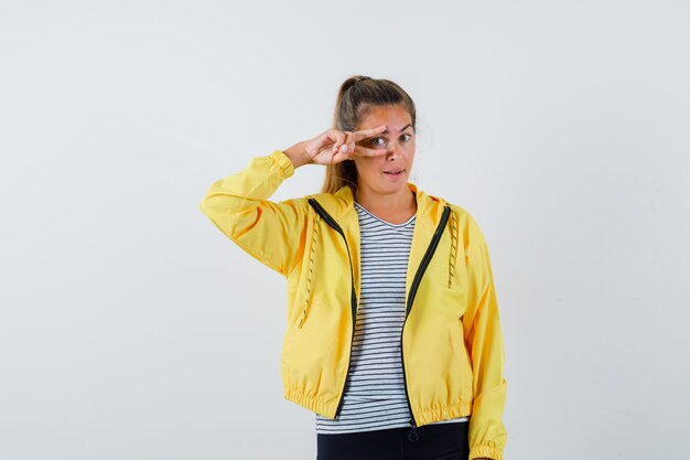 ジャケットを着た若い女性、目にVサインを示し、自信を持って見えるTシャツ、正面図。