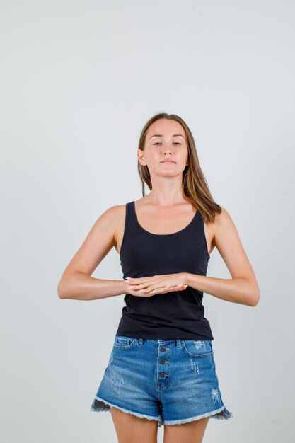 Young female joining two hands in black singlet, shorts and looking relaxed. front view.