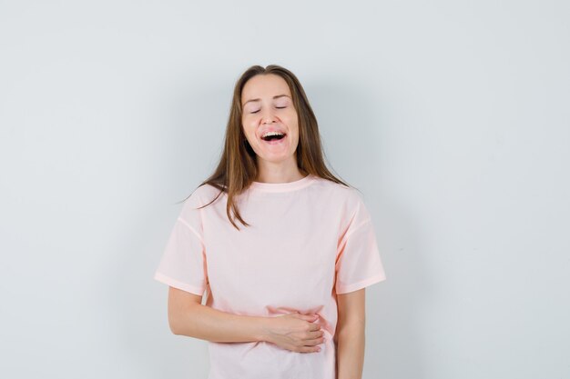 Young female keeping eyes closed in pink t-shirt and looking happy. front view.