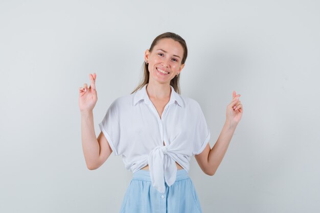 Young female keeping fingers crossed in blouse and skirt and looking glad