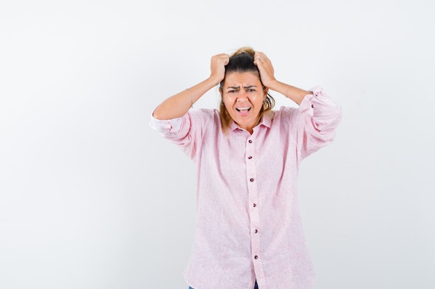 Young female keeping hands on head in pink shirt and looking wistful 