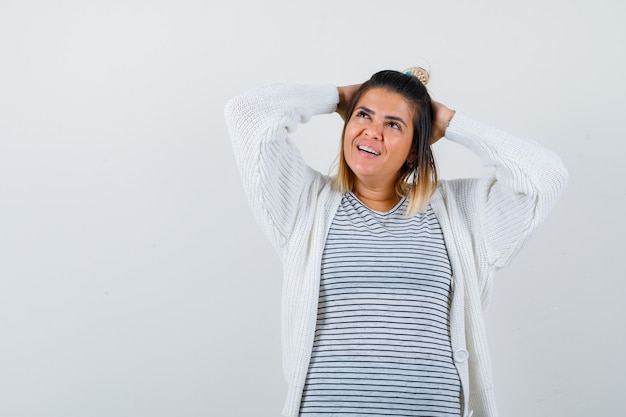 Tシャツ、カーディガンで頭の後ろに手を保ち、陽気に見える若い女性。正面図。