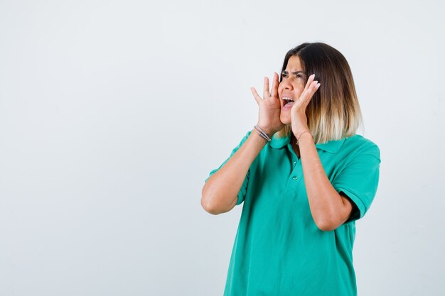 Young female keeping hands near mouth in polo t-shirt and looking scared. front view.