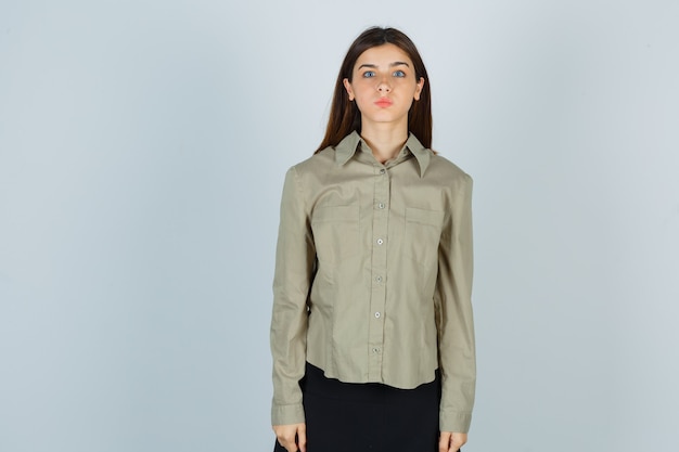 Young female keeping lips folded in shirt, skirt and looking puzzled. front view.