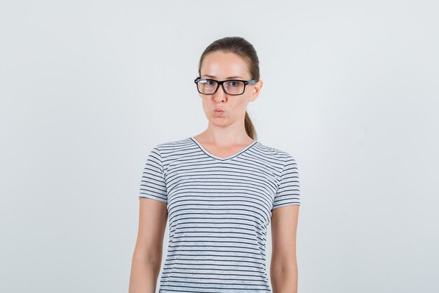 Young female keeping lips rounded in striped t-shirt, glasses front view.