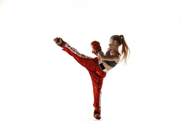 Young female kickboxing fighter training isolated on white wall. Caucasian blonde girl in red sportswear practicing in martial arts. Concept of sport, healthy lifestyle, motion, action, youth.