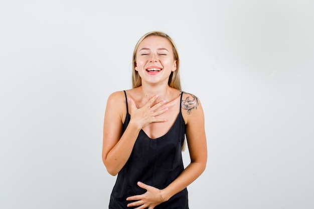 Young female laughing with hands on chest and stomach in black singlet and looking happy 