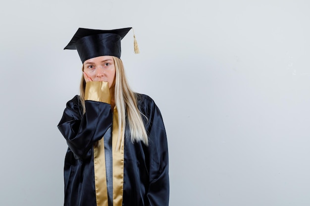 Young female leaning cheek on palm in graduate uniform and looking cute