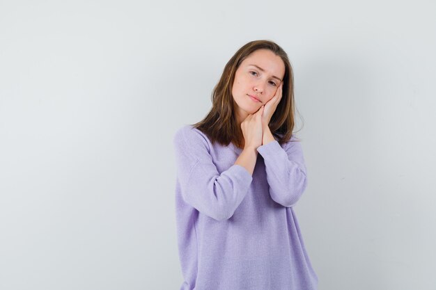 Young female in lilac blouse making pillow gesture and looking tired 