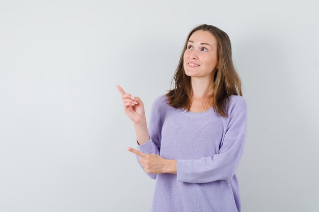 Young female in lilac blouse pointing up and looking focused 