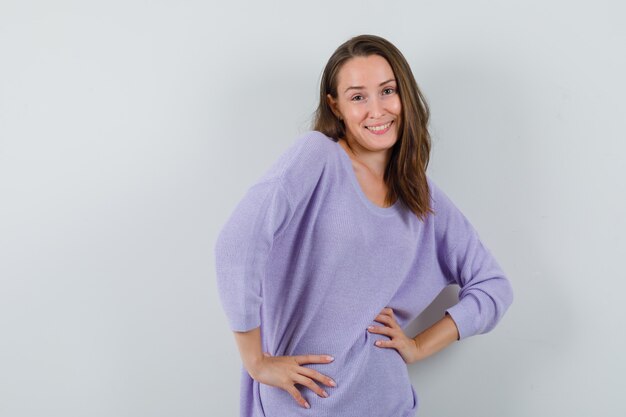 Young female in lilac blouse posing with hands on waist and looking charming 