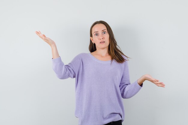 Young female in lilac blouse showing helpless gesture and looking helpless 