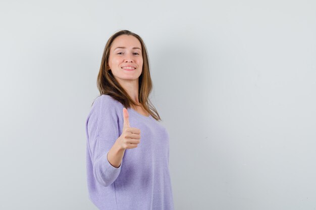 Young female in lilac blouse showing thumb up and looking glad 