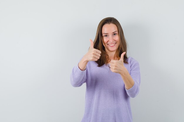 Young female in lilac blouse showing thumb up and looking pleased 