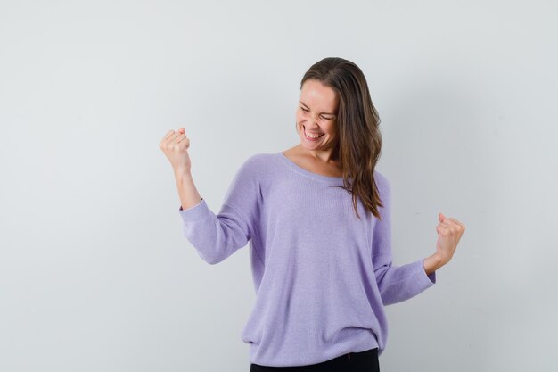 Young female in lilac blouse showing winner gesture and looking happy 