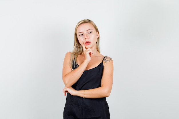 Young female looking aside with finger near mouth in black singlet and looking careful.