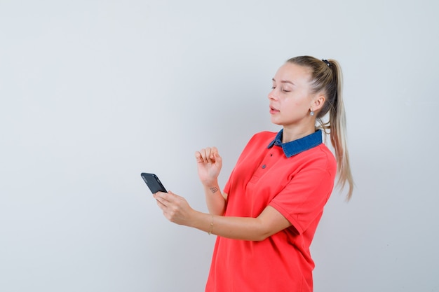 Молодая женщина, внимательно глядя на мобильный телефон в футболке, вид спереди.