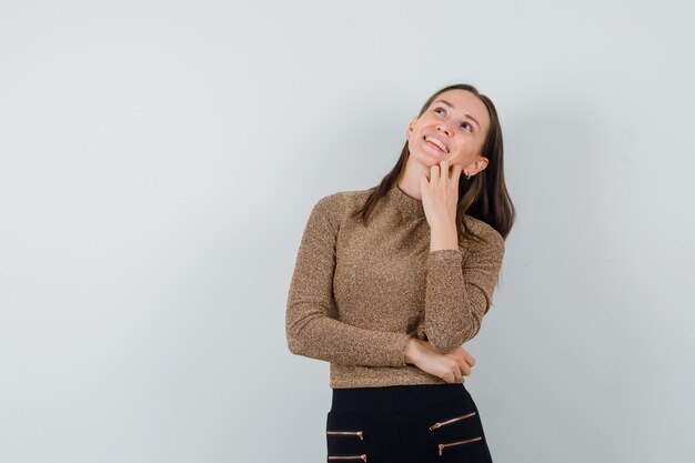 Young female looking away while smiling in golden blouse and looking cute , front view. space for text